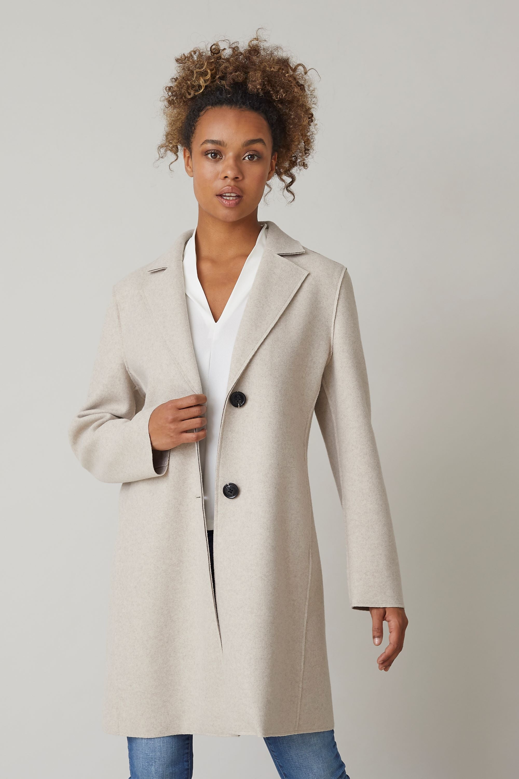 Woman wearing an elegant ivory ladies spring coat with a tailored fit, styled with jeans - perfect for a timeless spring look.
