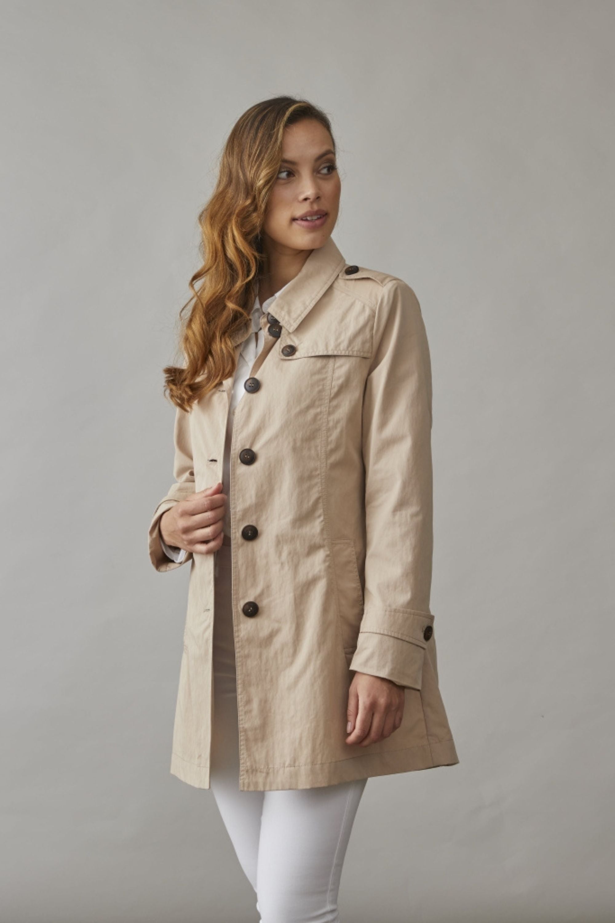 Woman wearing a short trench coat in sand, styled with white pants and a shirt, perfect for a timeless and elegant spring look.