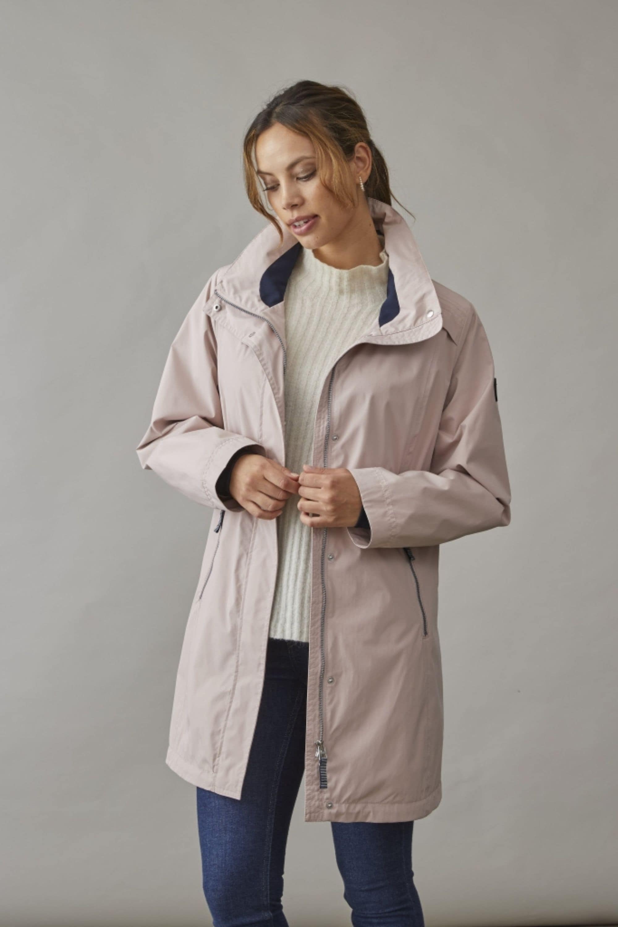 Woman wearing a lightweight spring jacket in soft rose, styled with a knitted sweater and jeans for a casual yet chic seasonal look.